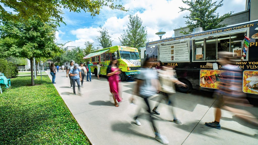 students walking by food trucks on campus